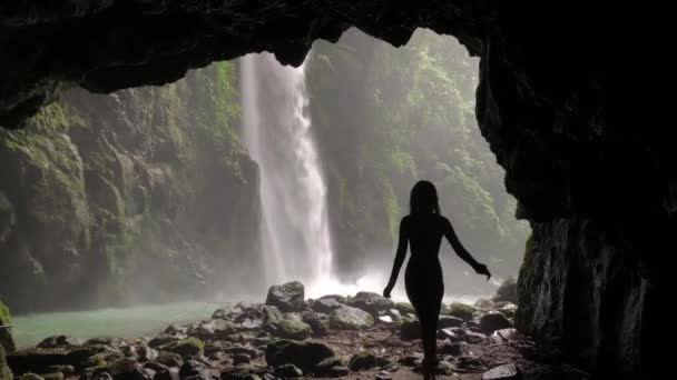 Silueta ženy kráčející v jeskyni v deštném vodopádu. — Stock video