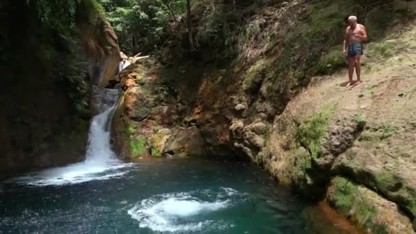 Une jeune femme et un vieil homme sautant dans une cascade tropicale en été. — Video