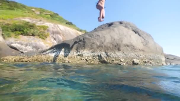 Una joven despreocupada salta de la roca al océano azul en el día de verano . — Vídeos de Stock