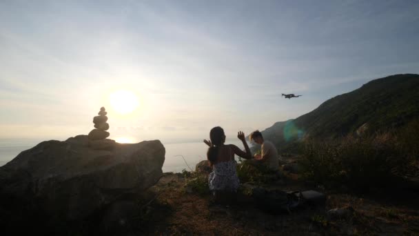 Молодая пара путешественников летающих дрон на скале горы море. — стоковое видео