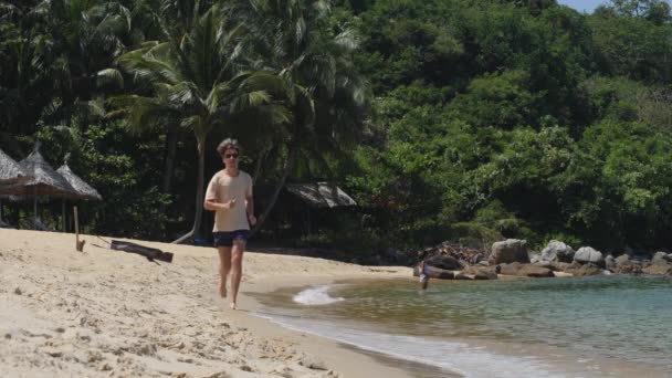 Молодий чоловік біжить на пляжі в літній день на райському острові . — стокове відео