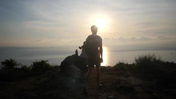 Пара путешественников на скале с видом на восход солнца и океан. — стоковое видео
