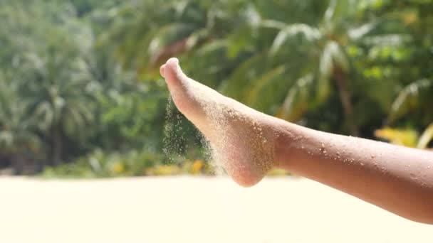 Close up of sandy feet on summer day, tropical trees in soft-focus background. — Stock video