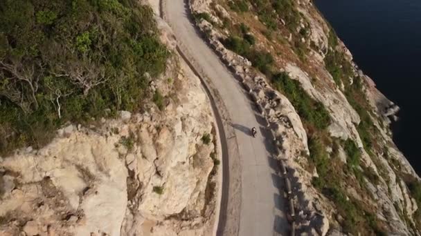 Shora dolů letecký pohled na motoristu jedoucího po nebezpečné silnici podél útesu. — Stock video