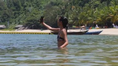 Bikinili güzel, mutlu bir kadın. Banyo yapıyor ve denizde selfie çekiyor..