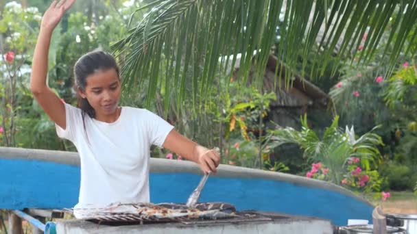 庭で魚を焼きながら踊る若い女性. — ストック動画