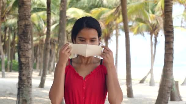 Ung asiatisk kvinna bär mask på stranden, palmer bakplats. — Stockvideo