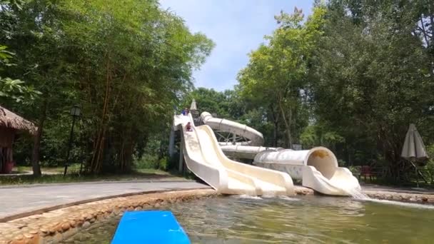 Un hombre y una mujer que monta la estera del tobogán acuático en un tobogán abierto en el parque acuático al aire libre. — Vídeo de stock