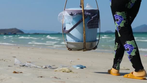 Крупним планом жінка, що носить ярмо, ходить на піщаному пляжі з пластмасами . — стокове відео
