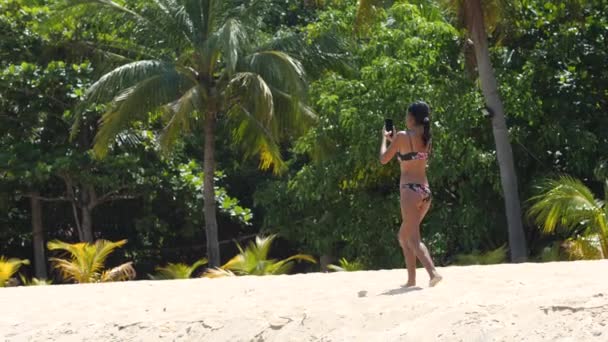 Młoda kobieta w bikini spacerująca po plaży w upalny dzień i kręcąca filmy. — Wideo stockowe