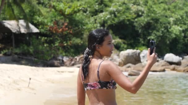 Vrouw met nat haar en in natte bikini filmen video 's tijdens het wandelen op het strand. — Stockvideo