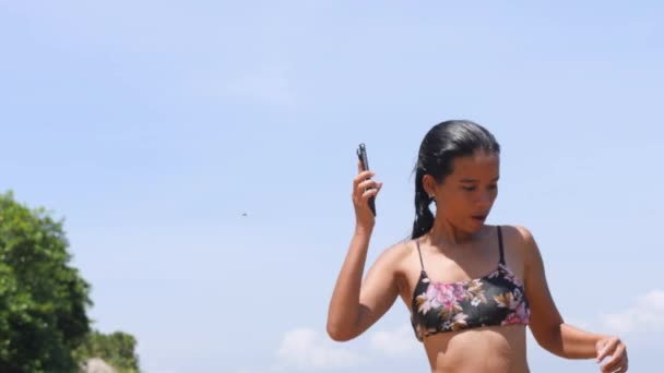 Wesoła młoda kobieta w bikini skacząca w wodzie na plaży w letni dzień. — Wideo stockowe