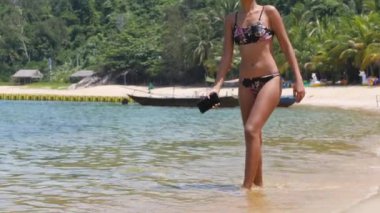 Sıcak yaz gününde, bikinili, kumsalda yürüyen minyon bir kadının ağır çekimleri..