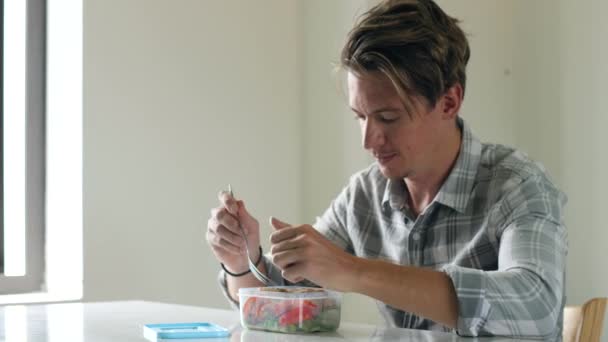 Un joven comiendo ensalada de verduras caseras saludables en una lonchera en casa. — Vídeo de stock