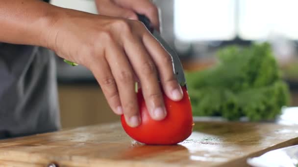 Unga kvinnor händer skivning färsk röd tomat på en träskiva i köket — Stockvideo