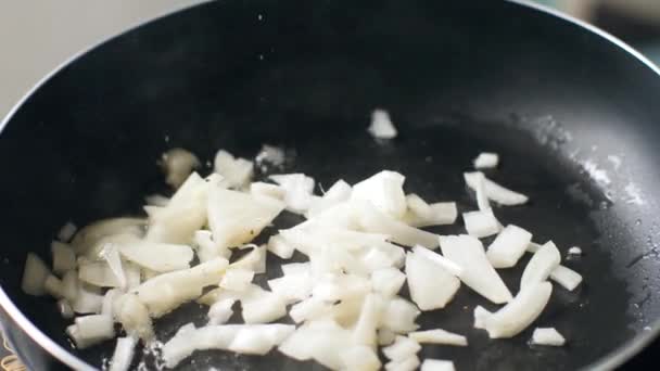 Närbild av varm stekpanna med olja och lök som tillsätts och sauteed av en kockhand. — Stockvideo