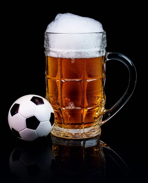 Bardak bira ve bir siyah arka plan üzerine izole bir küçük futbol topu.
