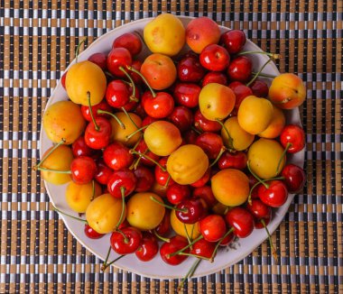 Çok olgun taze kayısı ve bambu peçeteye bir tabak içinde kiraz.