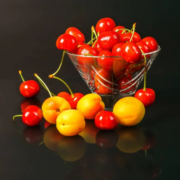 Reife frische Aprikosen und Kirschen in einer transparenten Glasvase auf dunklem Hintergrund. — Stockfoto