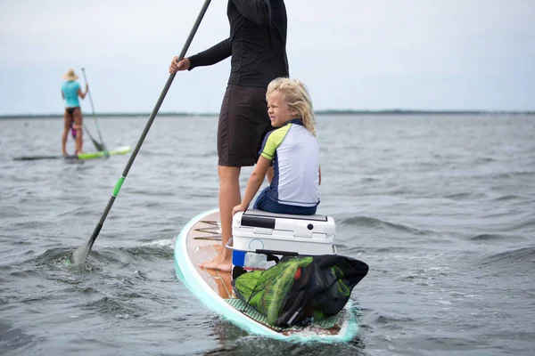 一个女人和一个小男孩坐在船桨板上 另一个男人在远处划桨 — 图库照片