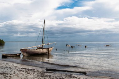 Bulutlu gökyüzü ve sığınağın Kano çevreleyen ile sakin su ile mafya Adası, Tanzanya, sunrise plajda su üzerinde küçük Ahşap Yelkenli.