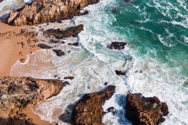 Top view of a shoreline with turquoise sea, white waves and rocks. clipart