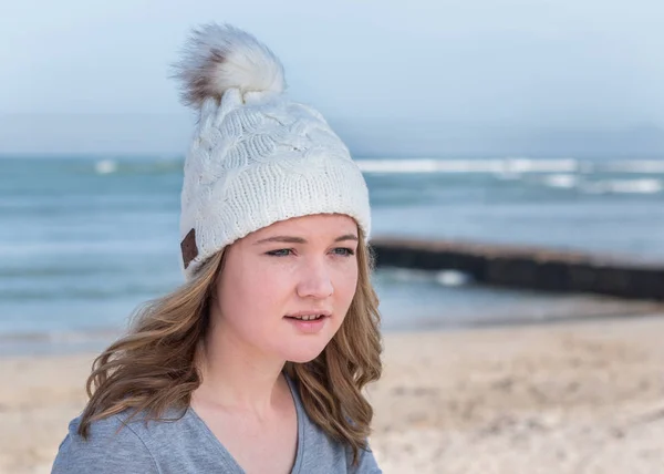 Female model wearing white knitted beanie with Bluetooth speakers inside, listening to music outdoors.