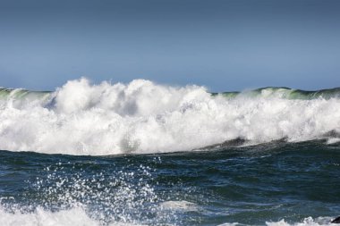 Güçlü Okyanus Dalgası Beyaz Su Köpüğüyle Kırılıyor ve Açık Mavi Gök Burnu Altında Vahşi Deniz 'de Süzülüyor
