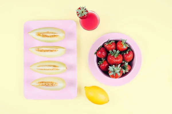 Čerstvé jahody v misce a melone na pastelové žluté pozadí. — Stock fotografie