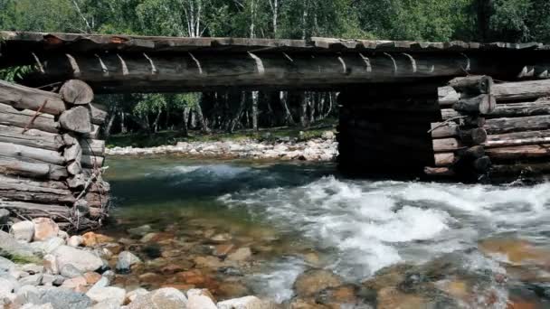 Fiume di montagna che scorre sotto un ponte di legno scenografico. Un fiume con un fondo di pietra. Rapido corso di un fiume di montagna. Sparatoria statica . — Video Stock