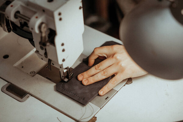 Close up of sewing machine working part with leather. The masters hands sews a leather product. Handmade concept.