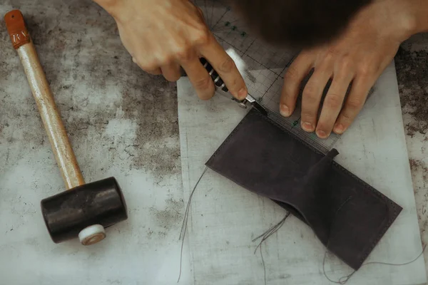 Close up of leather craftsman working with natural leather and tools. Handmade master at work in local workshop. Leather wallet stitch. Top view