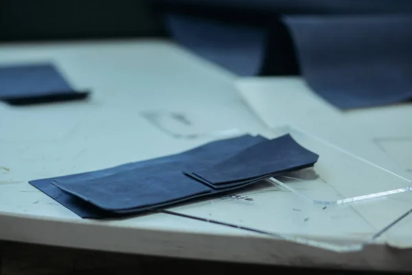 Dokonywanie skórzane portfele na maszynę do szycia przez rzemieślnika na stół biały. W pobliżu znajdują się kilka gotowych skórzane portfele. Na stole jest lampa i maszyny do szycia. — Zdjęcie stockowe
