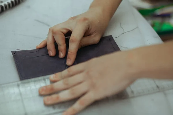 Ручной кожаный ремесленник делает бумажник, используя кусок натуральной кожи на своем рабочем месте с инструментами, закрыть фотографию его рук — стоковое фото