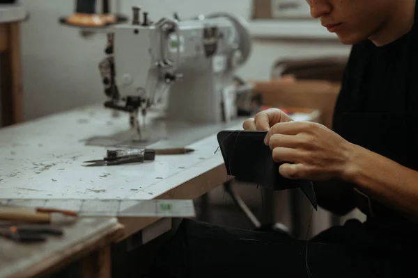 Close up of leather craftsman working with natural leather and tools. Handmade master at work in local workshop. Leather wallet stitch.