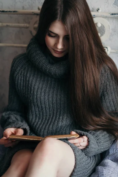 Vacker kvinna hemma sitter på en säng läsa en bok. — Stockfoto