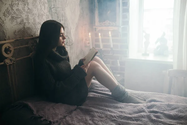 Young beautiful woman in warm sweater reading book on bed. — Stock Photo, Image