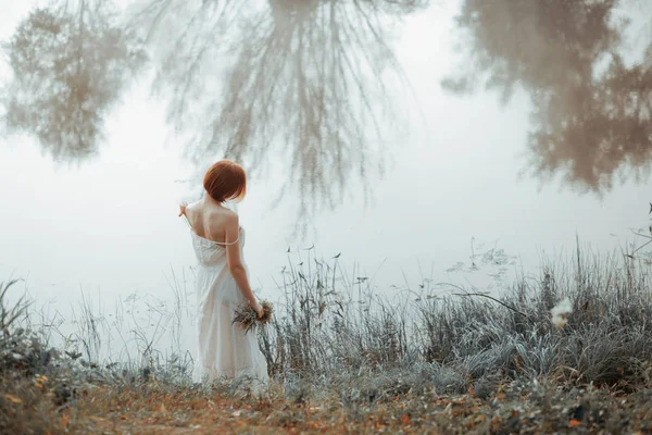 Women in white dress by river with plants in hand — Stock Photo, Image