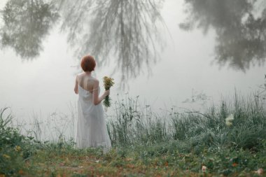 Sisli gölün yanında duran kızıl saçlı kadın