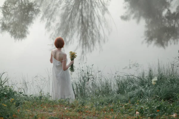 Kvinna med rött hår stående i närheten av dimmig sjö — Stockfoto