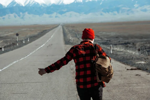 Facet w czerwonym autostopem jedzie samotną drogą. — Zdjęcie stockowe