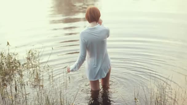 Chica con el pelo rojo de pie camisa vestida en el lago — Vídeos de Stock