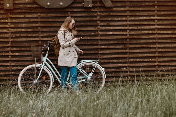Hübsches Mädchen schaut in ihr Handy neben einem Fahrrad — Stockfoto