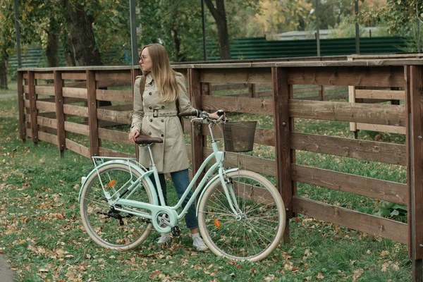 Hübsches Mädchen im Mantel steht mit ihrem Fahrrad — Stockfoto