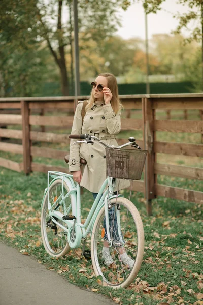 Симпатична дівчина в пальто і сонцезахисні окуляри біля велосипеда — стокове фото