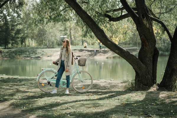 Flicka i päls och jeans stående med cykel framför speglande Lake — Stockfoto