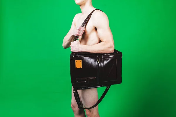 Naked fit guy in studio with leather bag