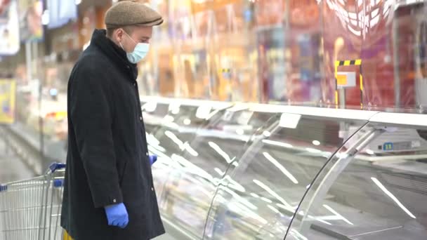 Человек в защитных перчатках и маске на пустых полках в супермаркете. — стоковое видео