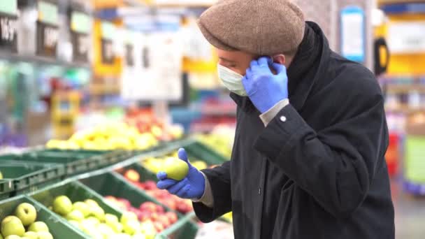 Un uomo in guanti protettivi e una maschera compra mele. — Video Stock