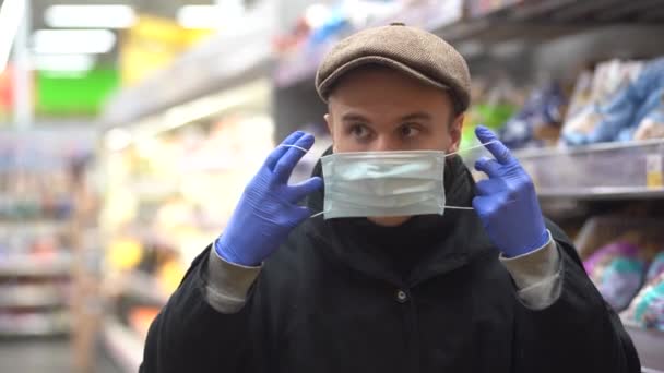 Şapkalı genç bir adam salgından korunmak için tıbbi maske takıyor. Markette yakın plan bir portre. Koronavirüs salgınından korunma — Stok video